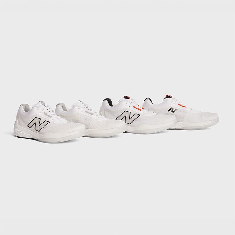 Men's and women's all white tennis shoes sitting on a grey background.