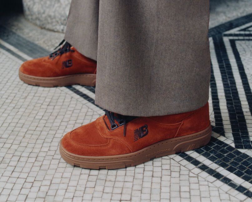 Knee down view of a man wearing a pair of New Balance Made in UK sneakers standing on a patterned tile floor.  