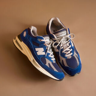 A pair of New Balance Made in UK sneakers in front of a rabbit in a brown textured studio environment. 