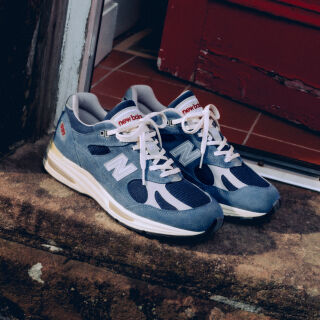 A pair of New Balance Made in UK sneakers on a white workbench surrounded by shoemaking tools and other textile equipment. 